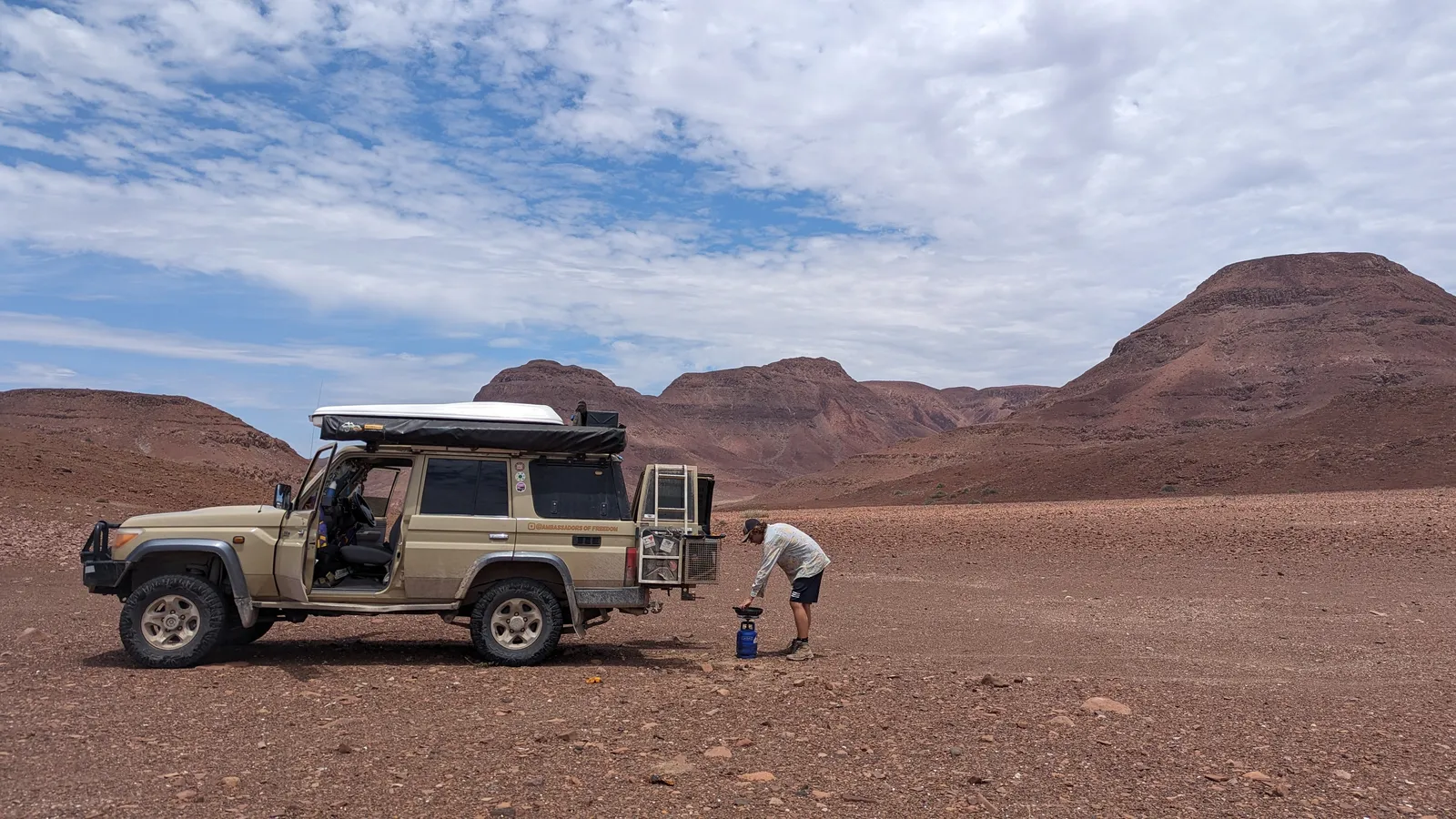 Mitchel met gespreide armen naast de Land Cruiser op een zoutvlakte